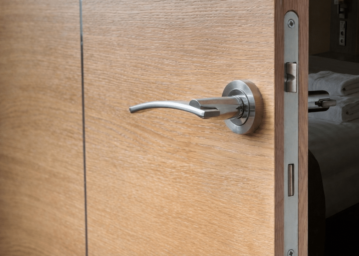 A wooden door slightly ajar reveals a modern room, featuring a sleek silver handle and glimpses of neatly folded towels inside.